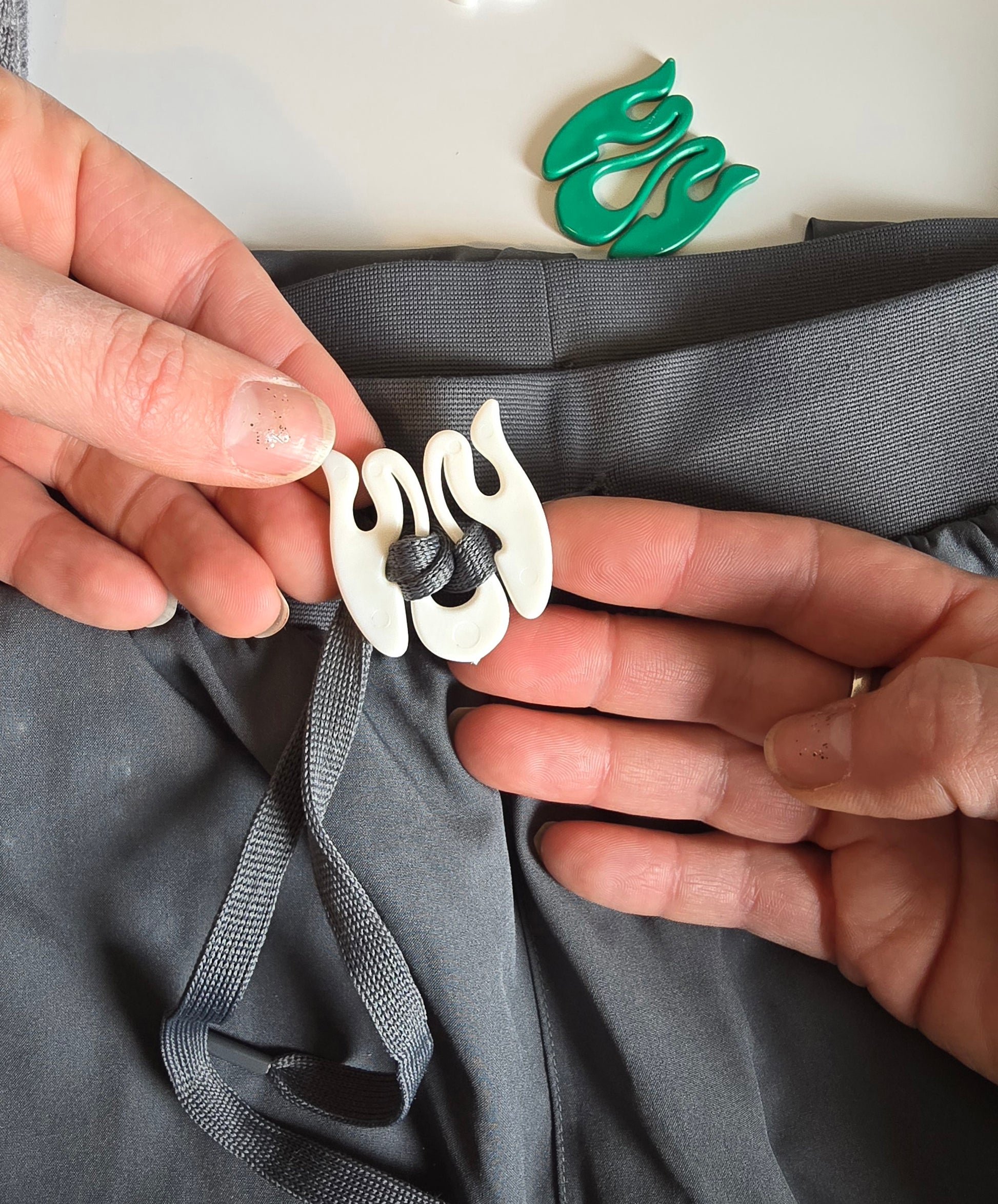 Person adjusting a white Wiggley String Tie on gray fabric with a green logo in the background.