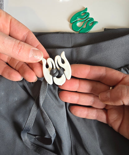 Person adjusting a white Wiggley String Tie on gray fabric with a green logo in the background.