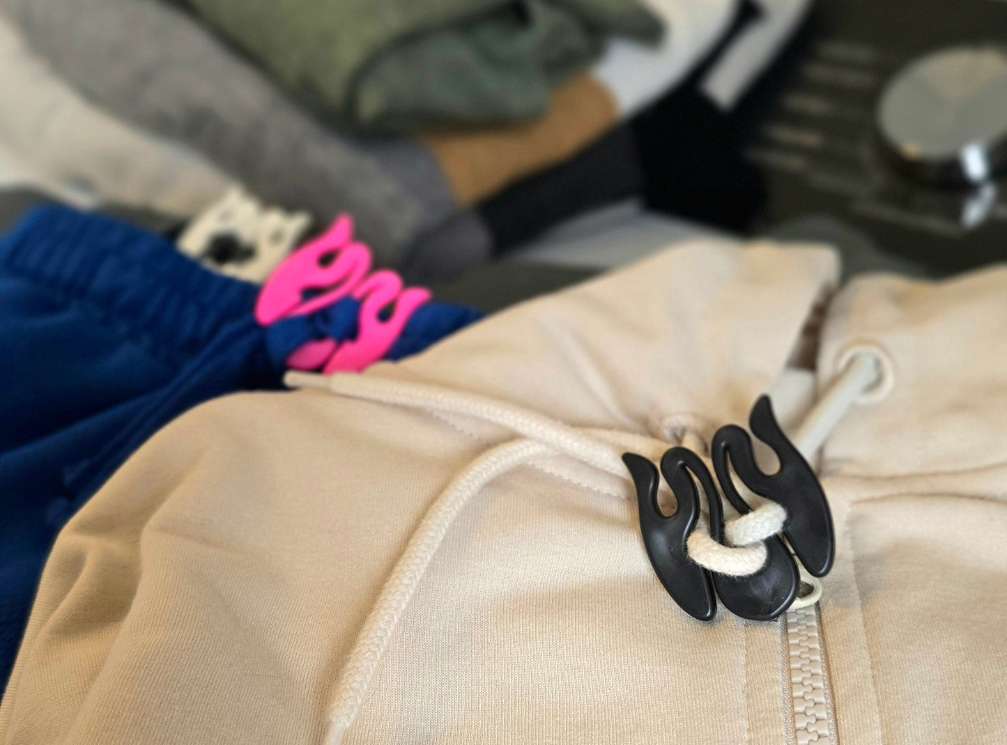 Close-up of a beige jacket with a Wiggley String Tie zipper and drawstring, with folded clothes in the background.